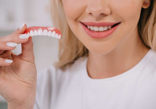 cropped-view-of-smiling-woman-holding-teeth-cover-2022-12-16-20-35-02-utc-min
